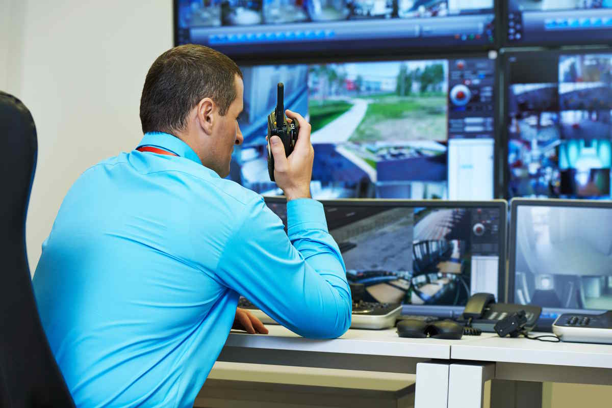 Security control room with a person monitoring multiple surveillance feeds while holding a radio.