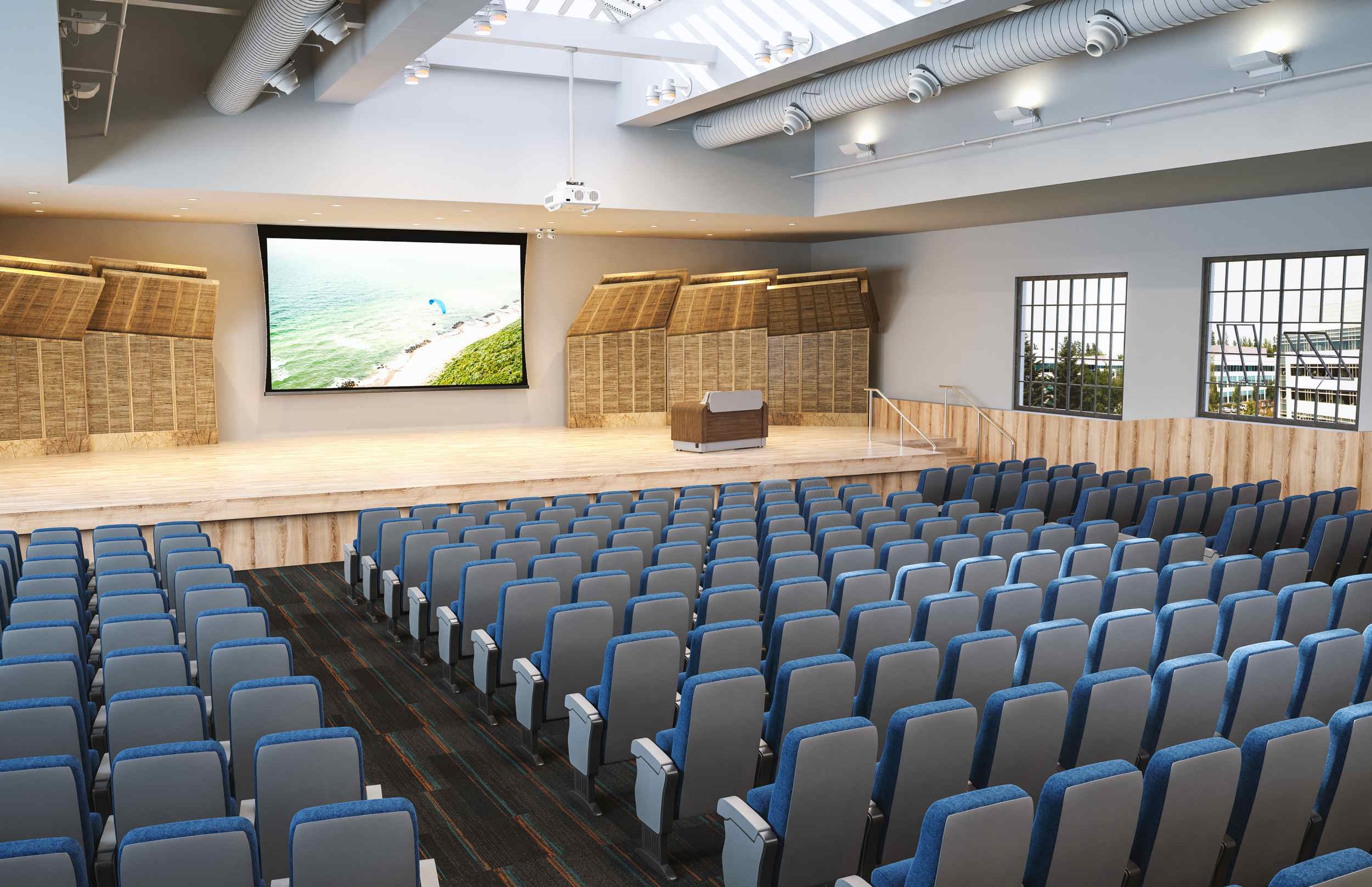 Modern auditorium with tiered blue seating facing a stage and a large screen showing a coastal scene.