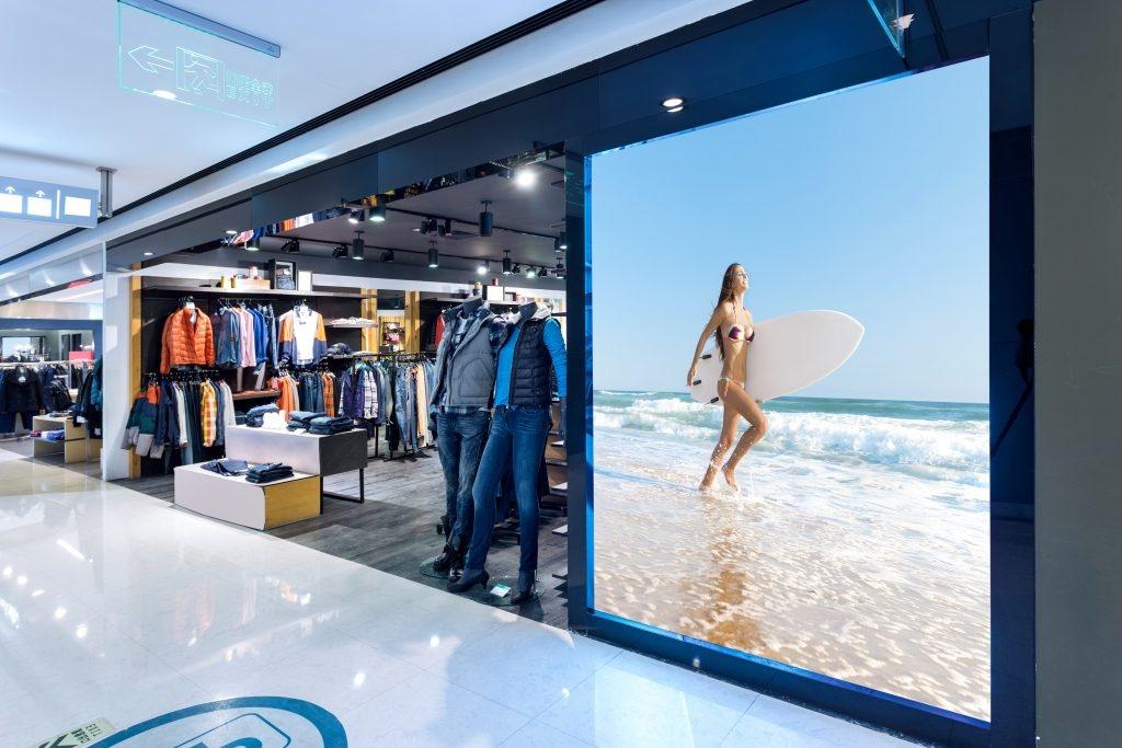 Modern clothing store with mannequins in casual outfits and a large beach‑themed ad display.