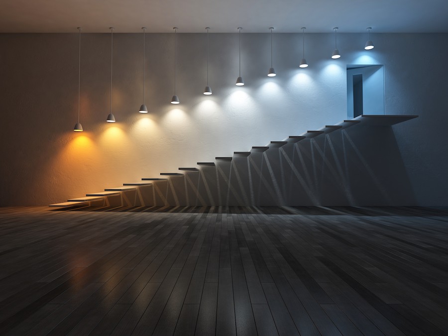 A staircase with 10 hanging lights above it, gradually changing in color from warm amber to cool blue light. 