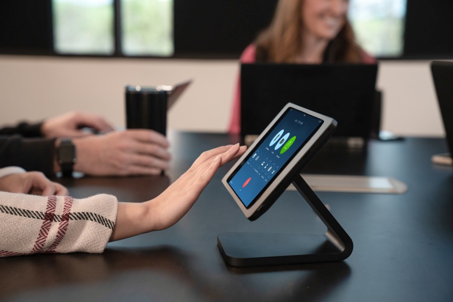 Woman’s hand tapping a touchscreen mounted on a conference room table. 