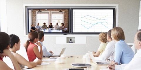 A table of people participate in a virtual meeting with conference room technology.