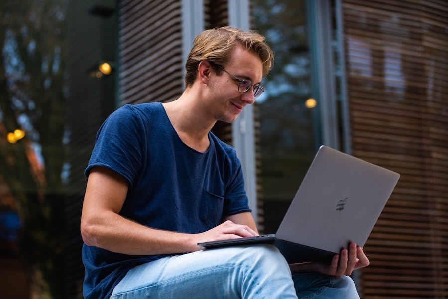 Blond man sitting outside on his laptop computer.