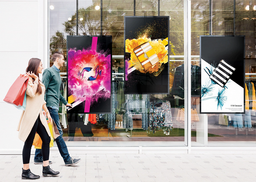 Three digital signs on a storefront with a man and woman walking by on the sidewalk.