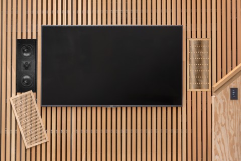 Wood-slatted wall with TV and two hidden James Loudspeakers beside it.