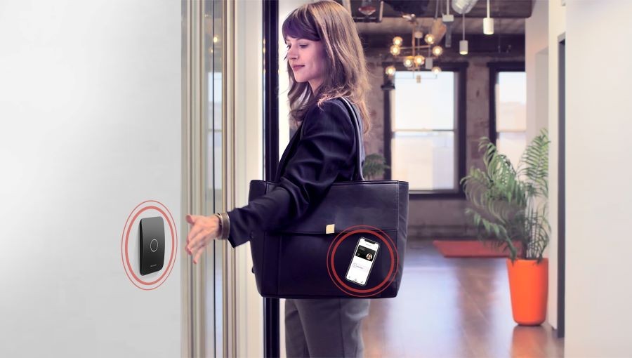 A woman waving her hand in front of an access control system. The system connects to the smartphone in her purse.