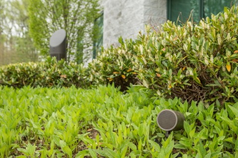 An outdoor speaker system with two speakers visible in a green backyard.