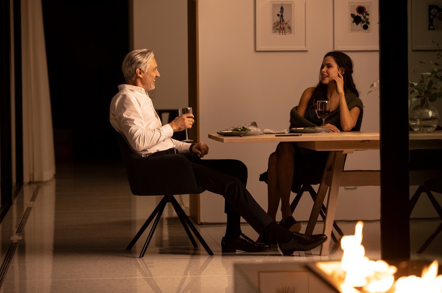 Man and woman sitting at a table drinking wine with warm lighting control illuminating the room.