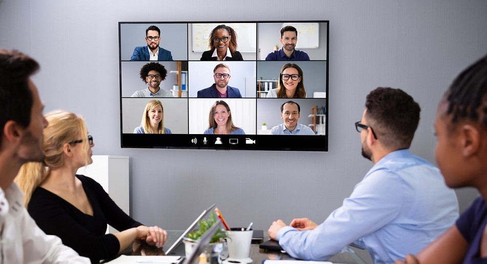 Four people sitting at a table video conferencing with coworkers over unified communication solutions.