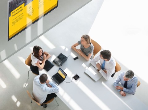 An overhead view of people working together at a table with laptops and a digital display.