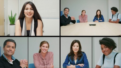 Four people in a conference room engaging in a video call with a woman in another room.