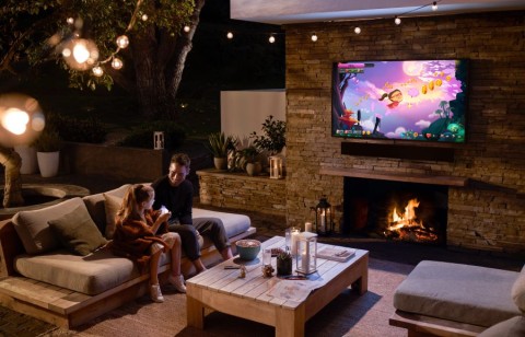 An outdoor area with a lit fireplace and a dad and daughter watching a cartoon on Samsung’s outdoor TV, The Terrace.