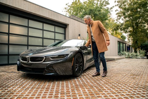 Man charging his electric vehicle in a driveway with a modern house in the background.