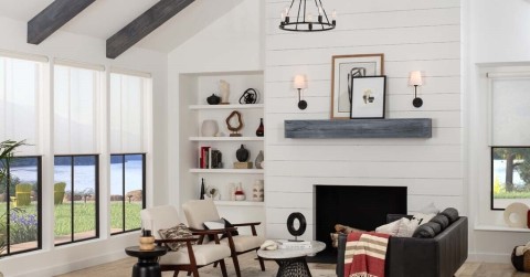 Bright, white living room with wooden beams and motorized shades on the windows. 