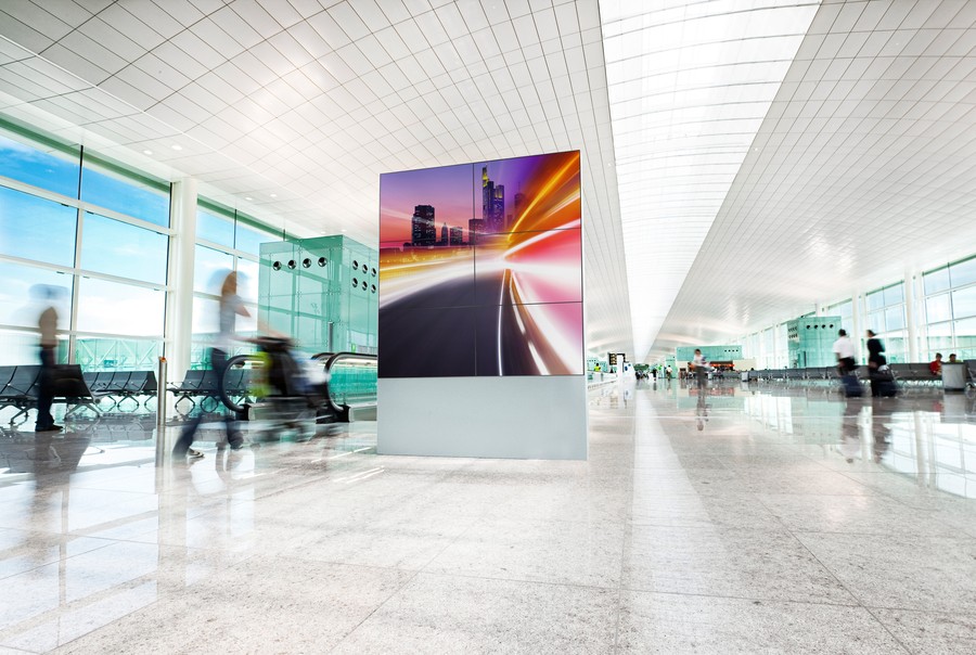 A white airport terminal with an LED video wall displaying a city landscape. 