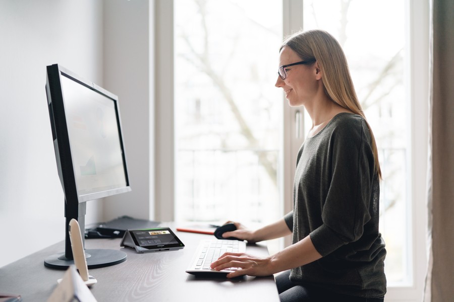 Woman in home office using a computer and tabletop console for video conferencing. 