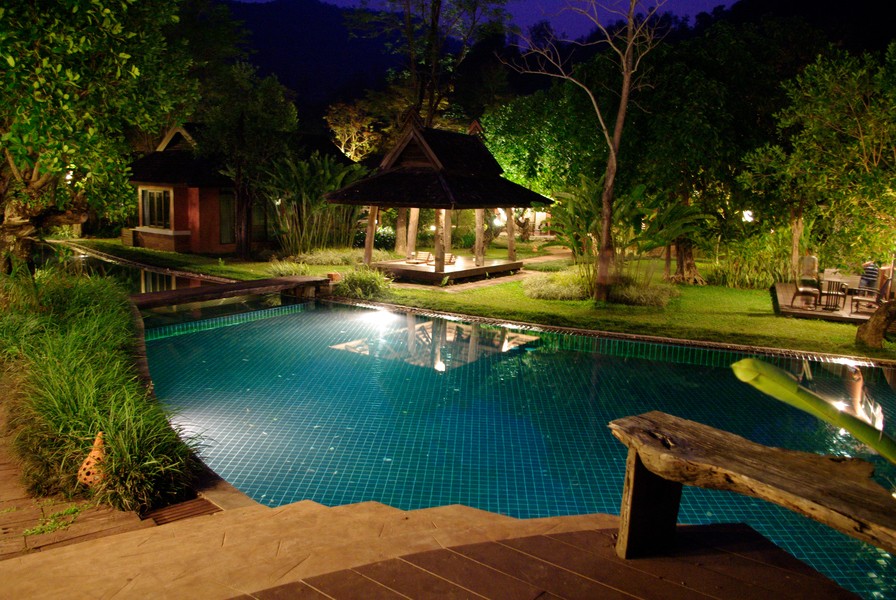 A backyard with a pool illuminated at night by a landscape lighting design.