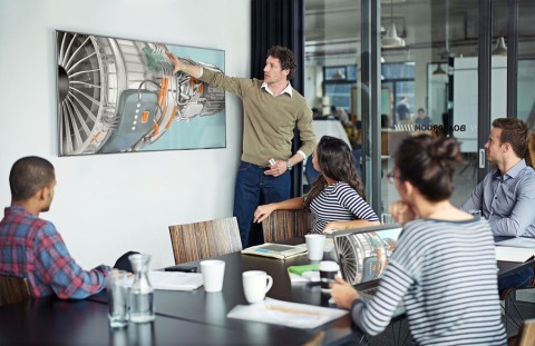 People in a conference room using a video display on the wall.