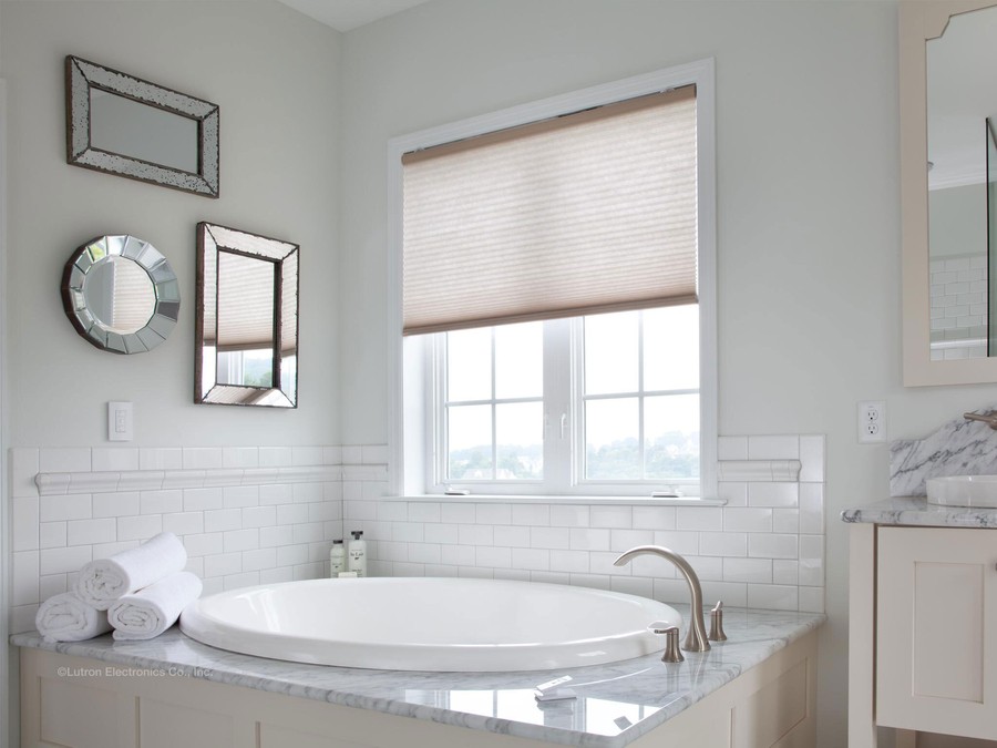 A bathroom with a circular tub and motorized shades on the window. 