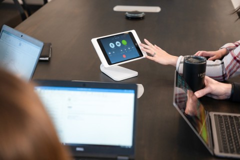 People at a conference table with laptops and a touchscreen conferencing controller.
