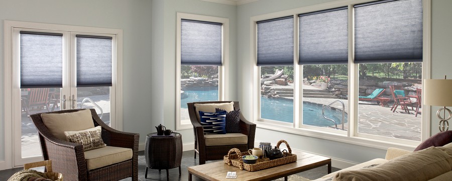 Living room with Lutron shades lowered a third down windows revealing an inground pool outside.