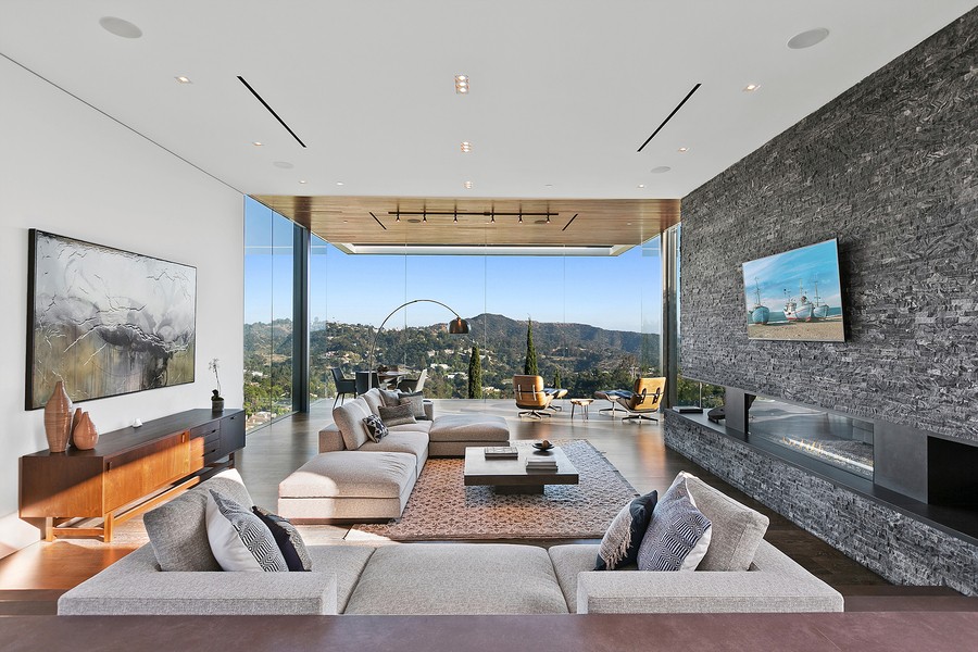 A living area with floor-to-ceiling windows, in-ceiling speakers, and a fire feature.