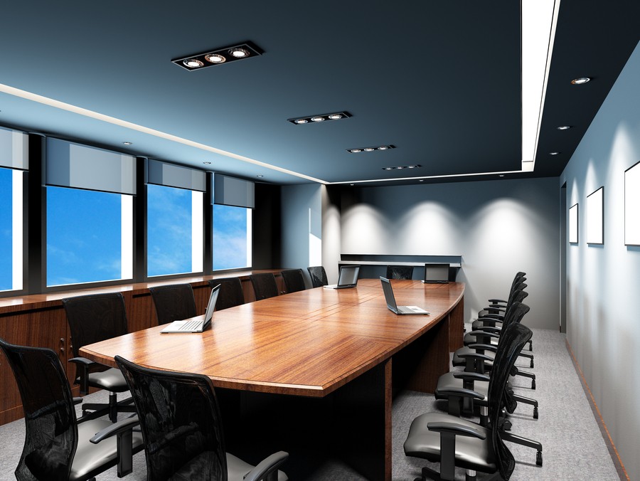 A meeting room with laptops, motorized shades, and soft illumination.