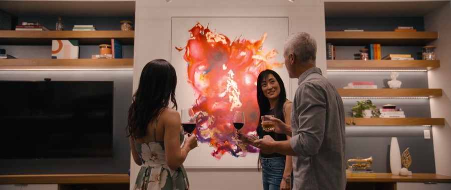 A group of people talking with wine. In the background is an abstract art piece and bookshelf illuminated by Ketra smart lighting.