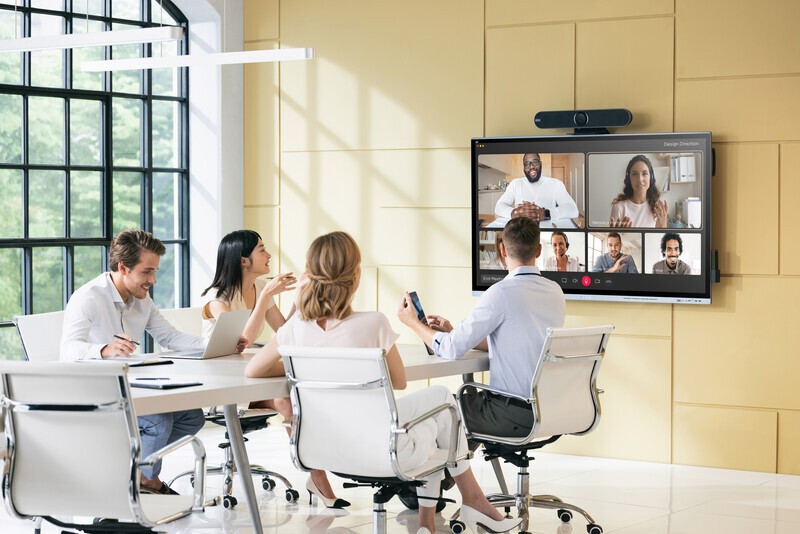 People at a conferencing table participating in a hybrid video call. 