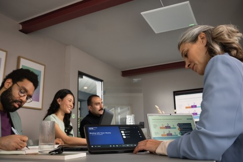 Group of people at a conference table using a tabletop controller to start a meeting with a Shure microphone above on the ceiling.