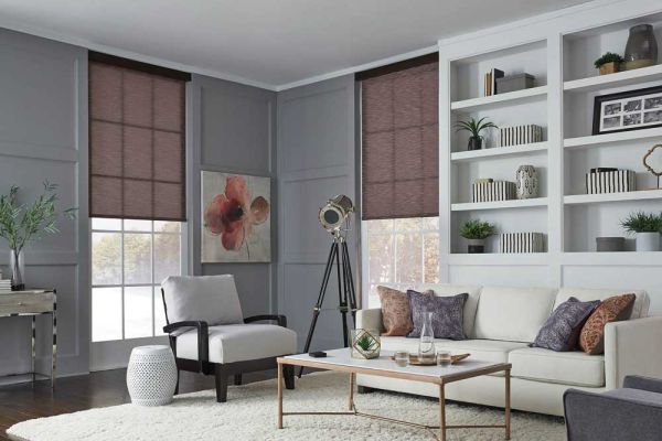 A bright living room with gray paneled walls, built-in shelving, and large windows. Furnishings include a white sofa, a black armchair, a tripod-style floor lamp, and a low coffee table, creating a cozy yet modern feel.