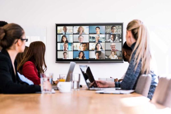 A modern conference room featuring a long table with ergonomic chairs, a large presentation screen mounted on the wall, and natural light streaming through expansive windows.